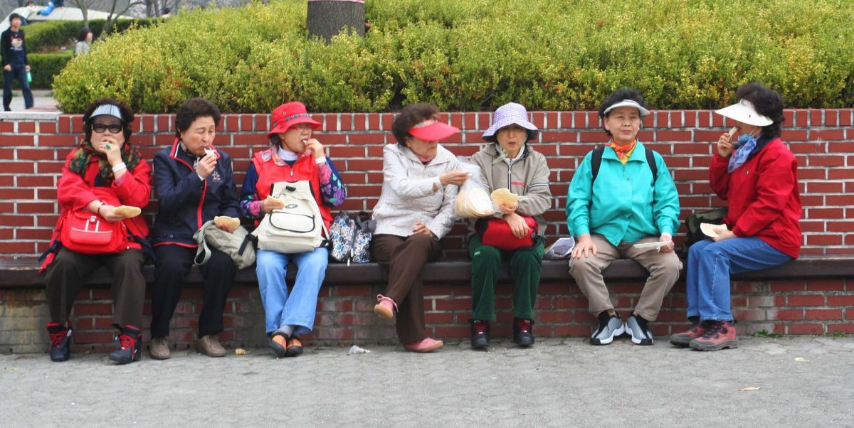 A group of Korean ajummas sitting together on a bench sharing a snack