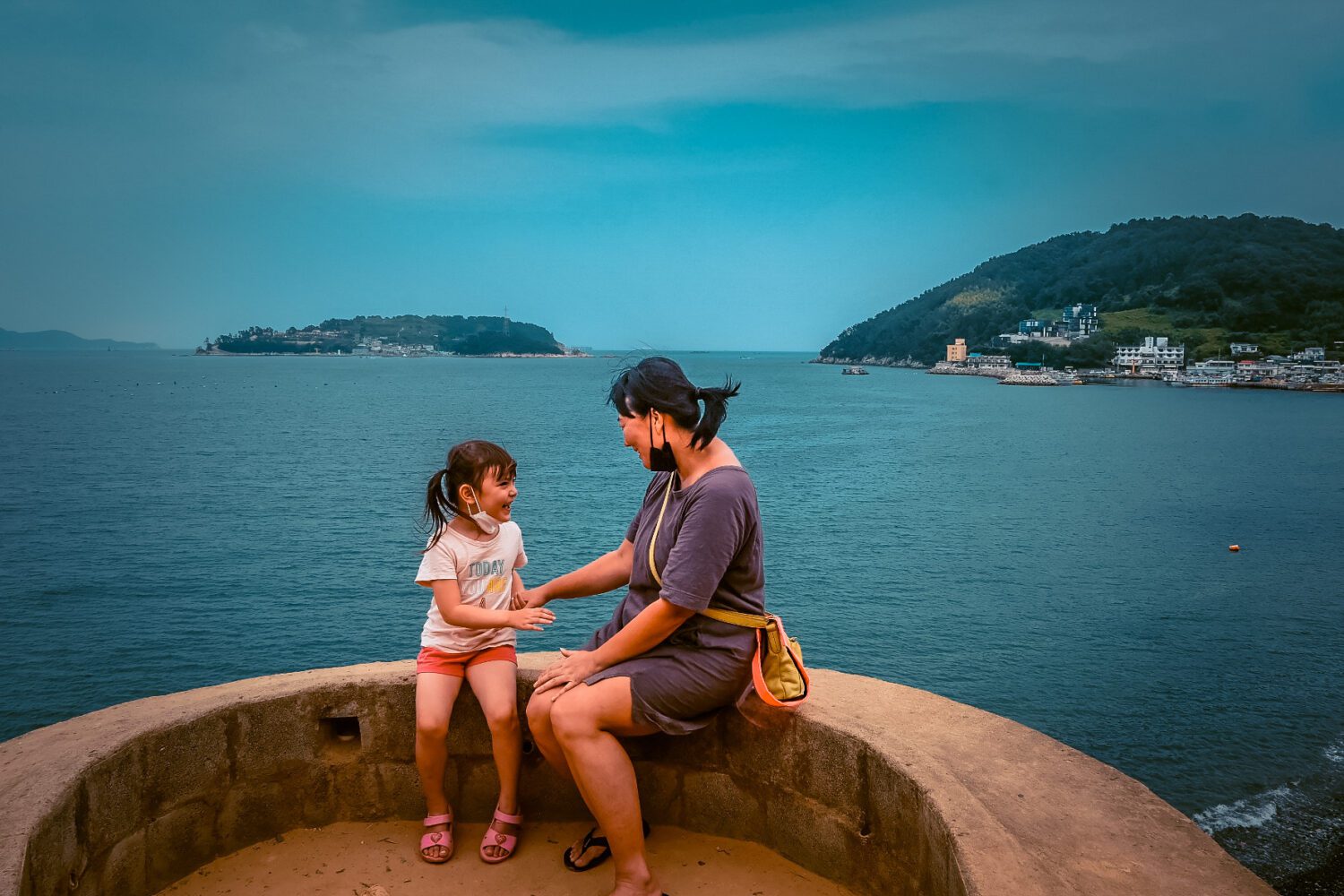 mom and daughter sitting on Maemiseong 메미성 with sea behind them